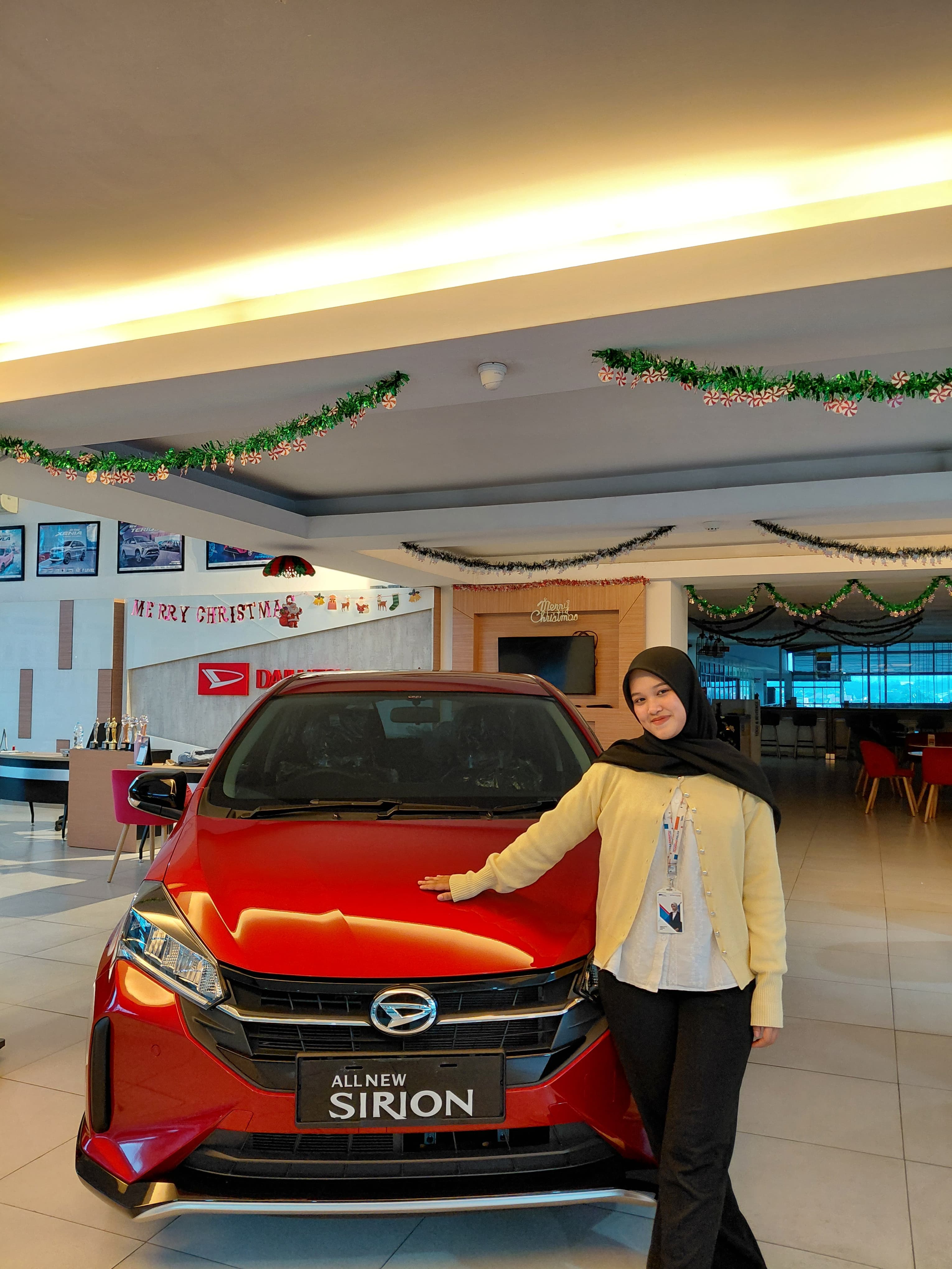 Sales Daihatsu berpose di samping All New Sirion merah di showroom